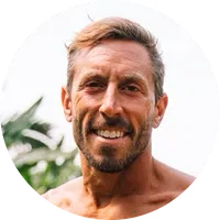 Smiling man with short hair outdoors, with greenery in the background.