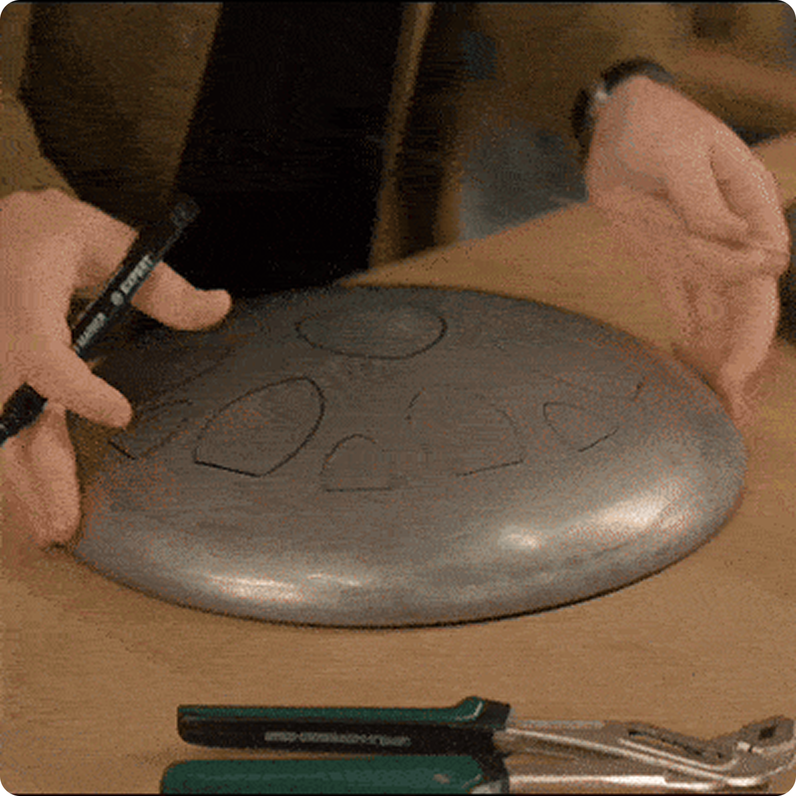 Person drawing on a metal handpan with a marker.
