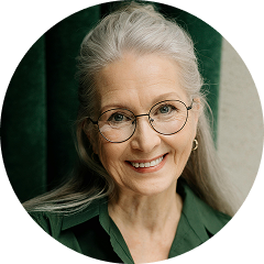 A smiling older woman with long grey hair and glasses, wearing a green shirt against a green background.
