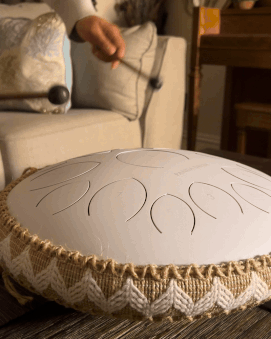 Person playing a handpan drum with mallets in a cozy room.