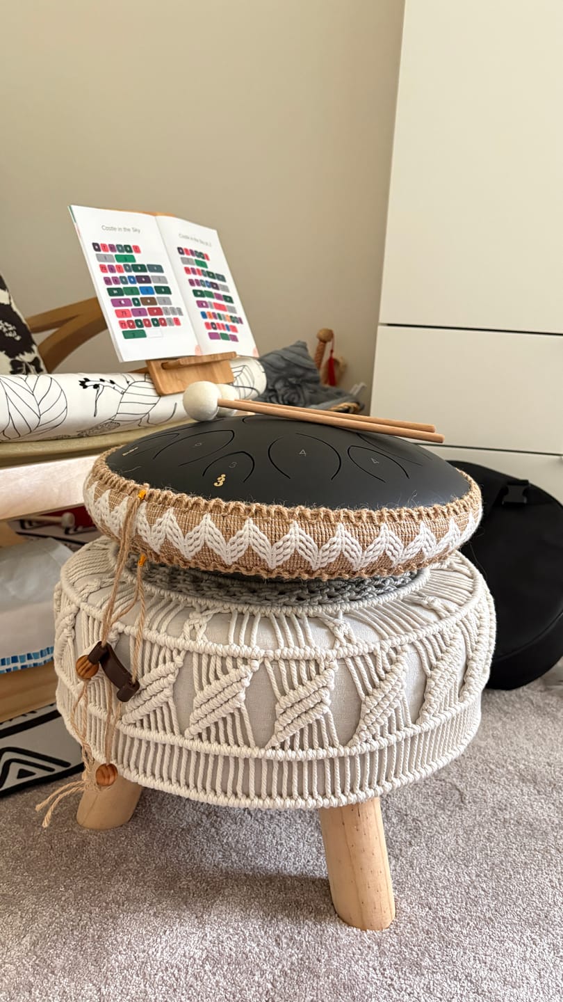 A handpan drum on a woven stool with a music book in the background.