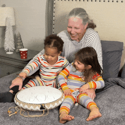 Three people in matching striped pajamas playing a round white instrument on a bed.