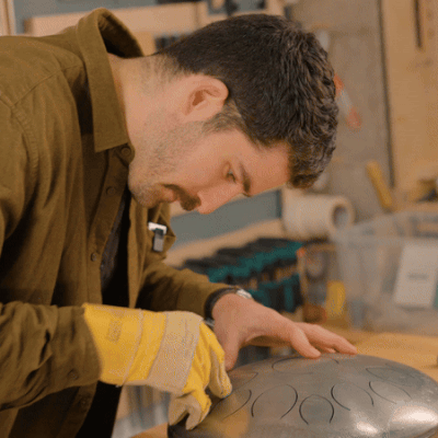 Person working on a metal instrument in a workshop.