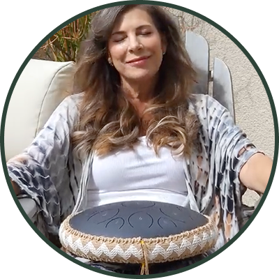 Woman sitting outdoors with a drum on her lap, eyes closed, smiling.