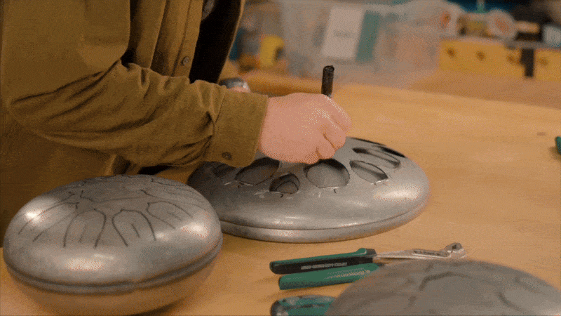 Person crafting metal tongue drums on a workbench.