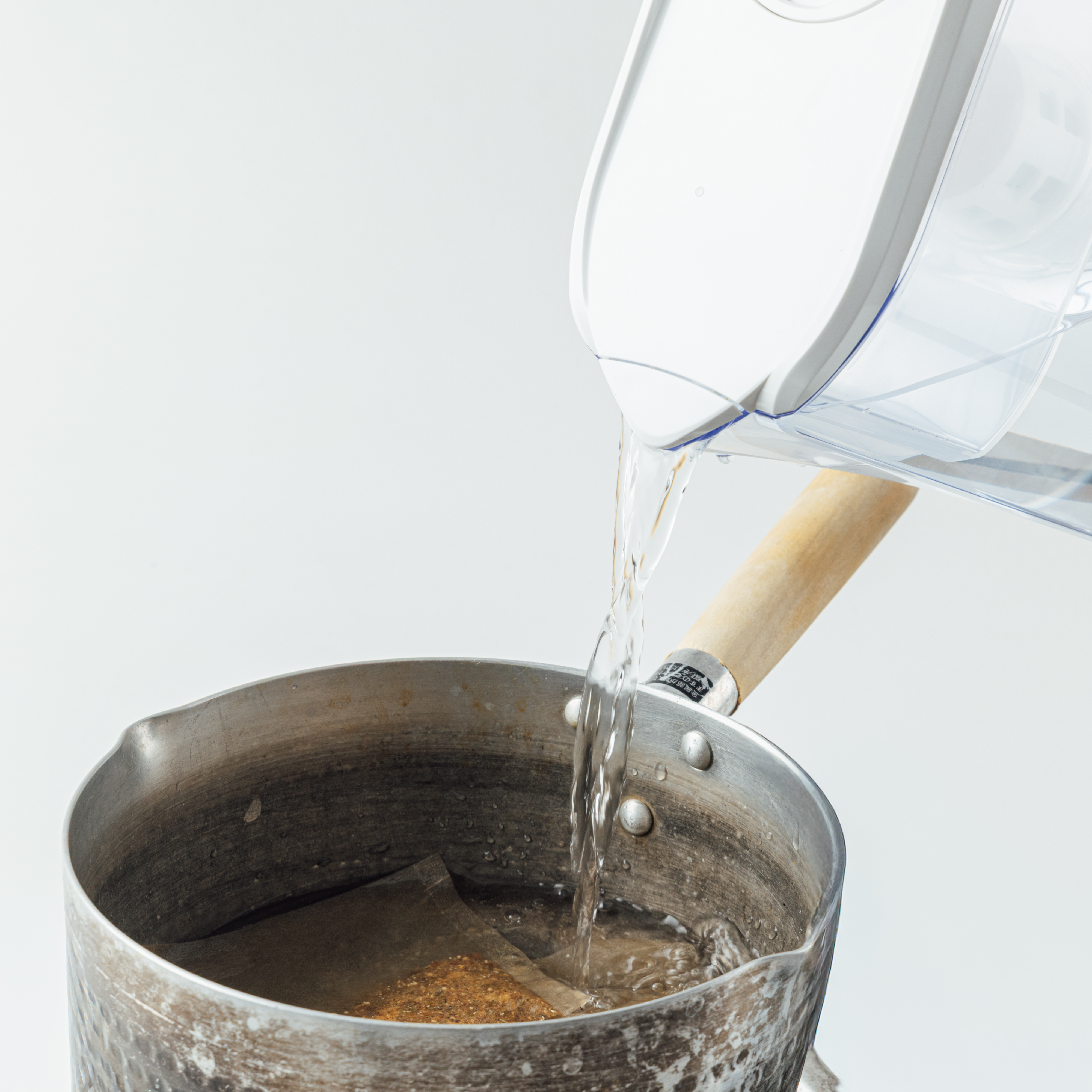 Water pouring from a filter pitcher into a metal saucepan containing a dashi or tea pack.