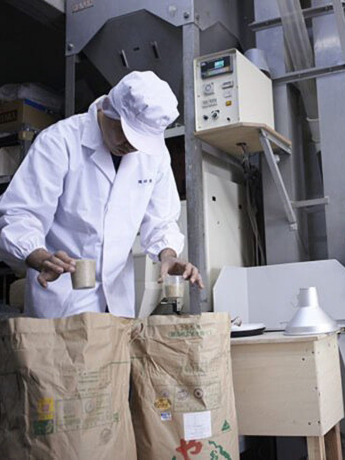 Person in white uniform examining contents over large paper bags in an industrial setting.