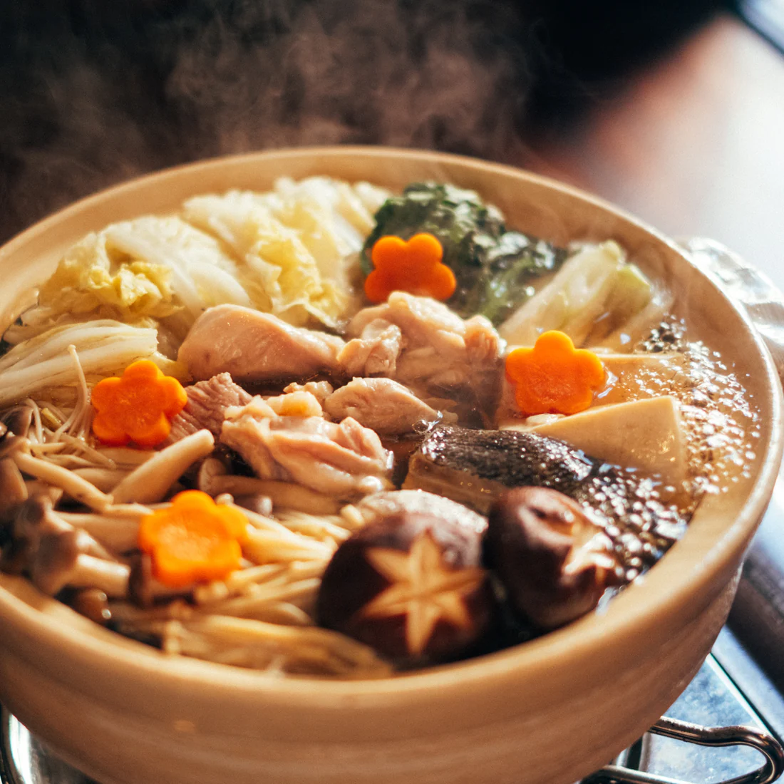 Steaming hot pot with vegetables, mushrooms, and meat, garnished with flower-shaped carrots.
