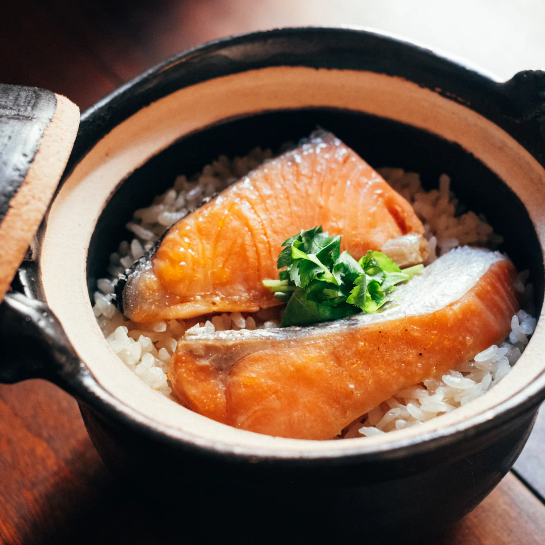 Two salmon fillets on rice in a ceramic bowl with greens.