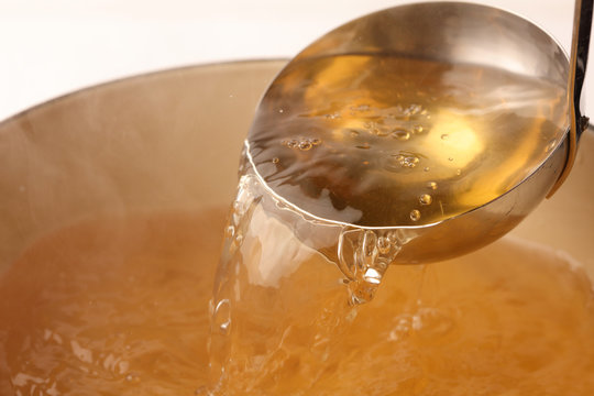 A ladle pouring clear broth into a pot.