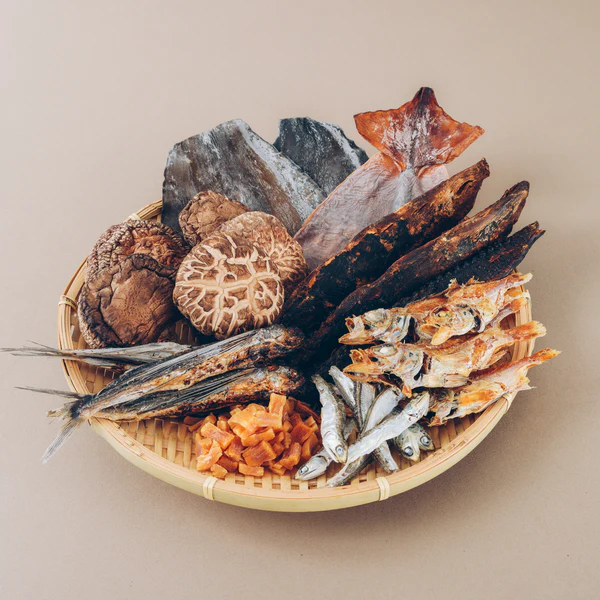 A bamboo basket containing assorted dried fish and mushrooms on a neutral background.