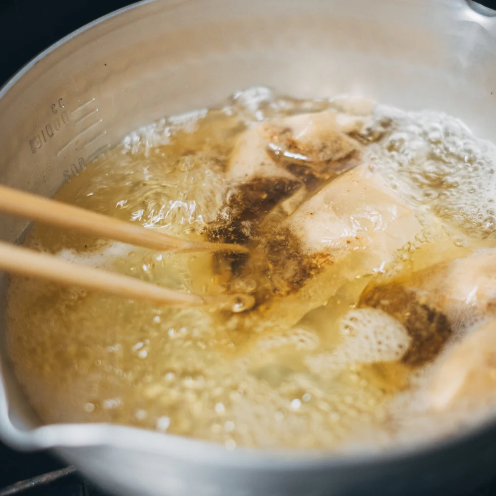 Food being fried in oil with chopsticks stirring.