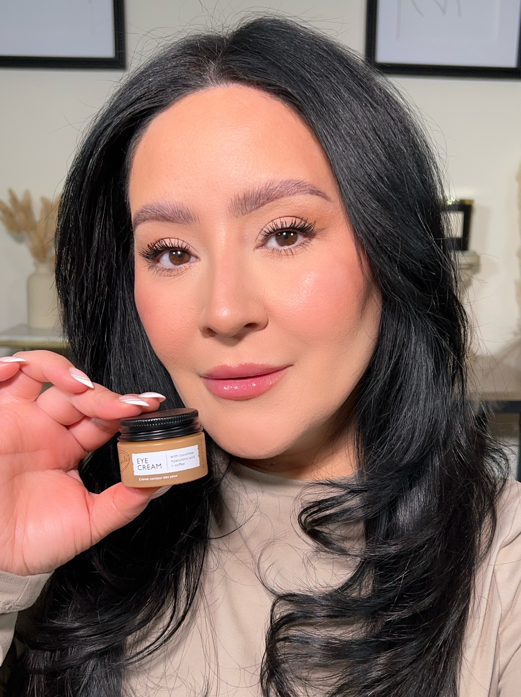 Person holding a small jar labeled 'Eye Cream' with a neutral expression.