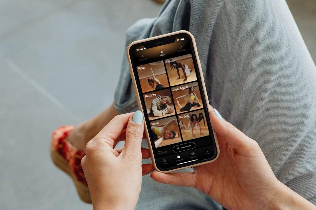 Person holding a smartphone displaying a fitness app with various workout categories.