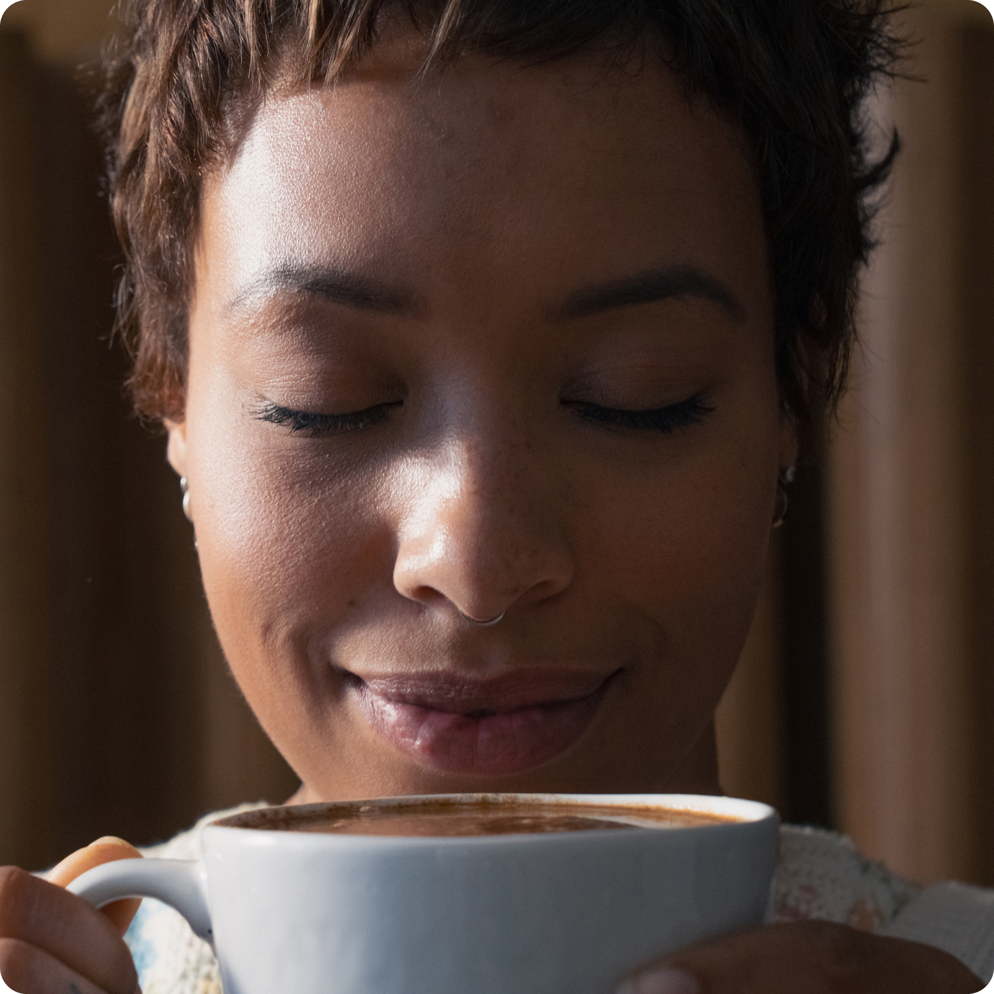 A close-up of a person with their eyes closed, smiling as they hold a white mug.