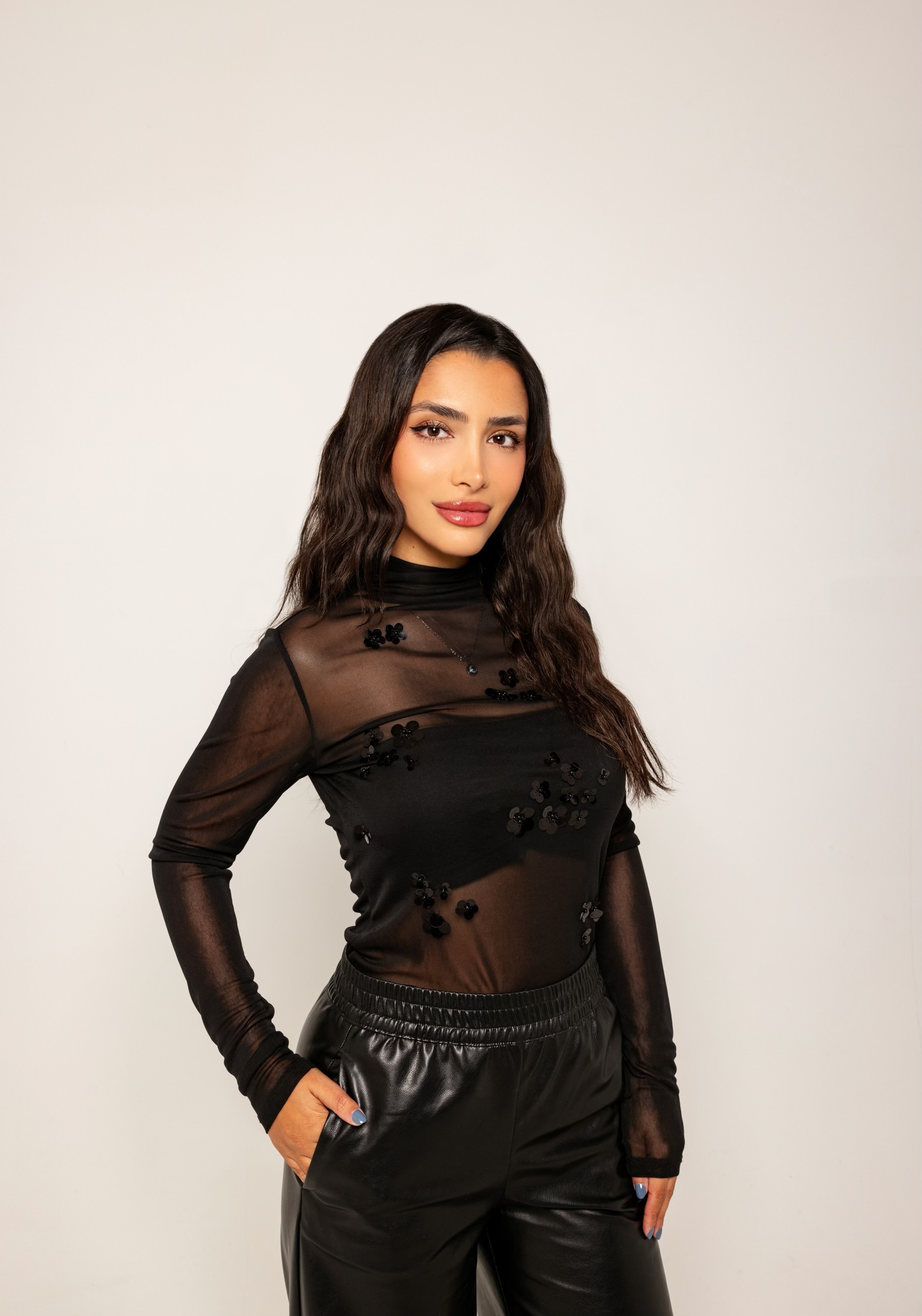 Person in black sheer top and leather pants against a plain background.