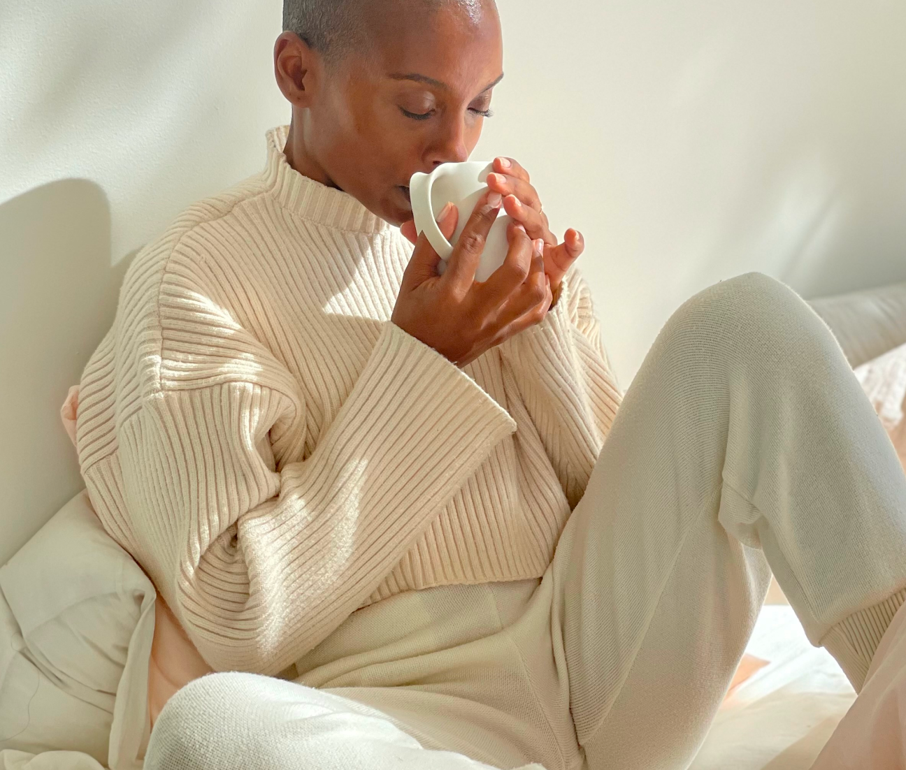 Person in cozy sweater sipping from a white mug.