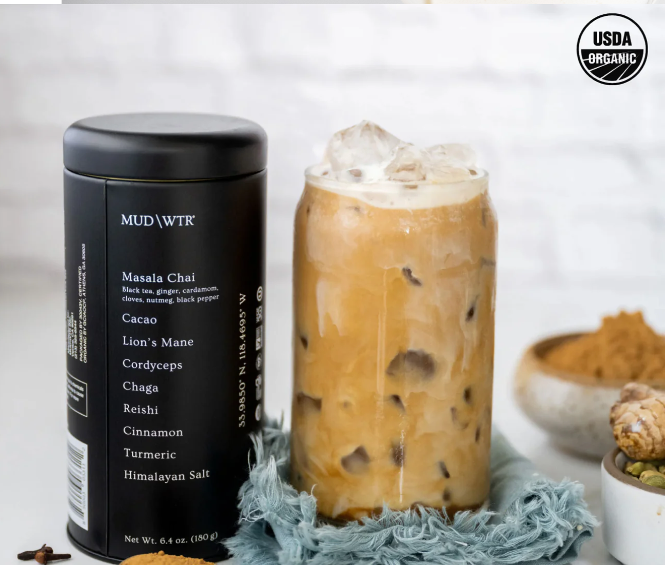 Can of MudWtr next to iced glass, jar of powder in background.
