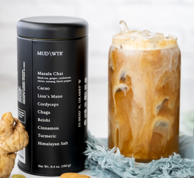 A canister labeled 'MUD\WTR' next to a glass of iced coffee with foam on top.