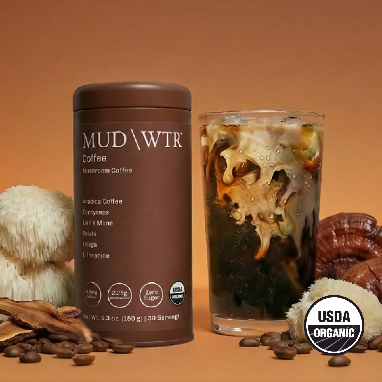 A can of MUD\WTR mushroom coffee next to a glass of iced coffee, surrounded by mushrooms and coffee beans.