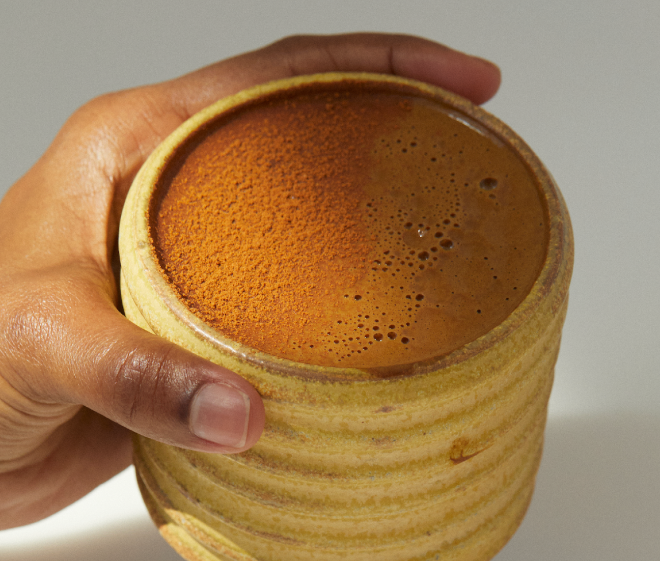 Hand holding a ceramic cup filled with foamy liquid.