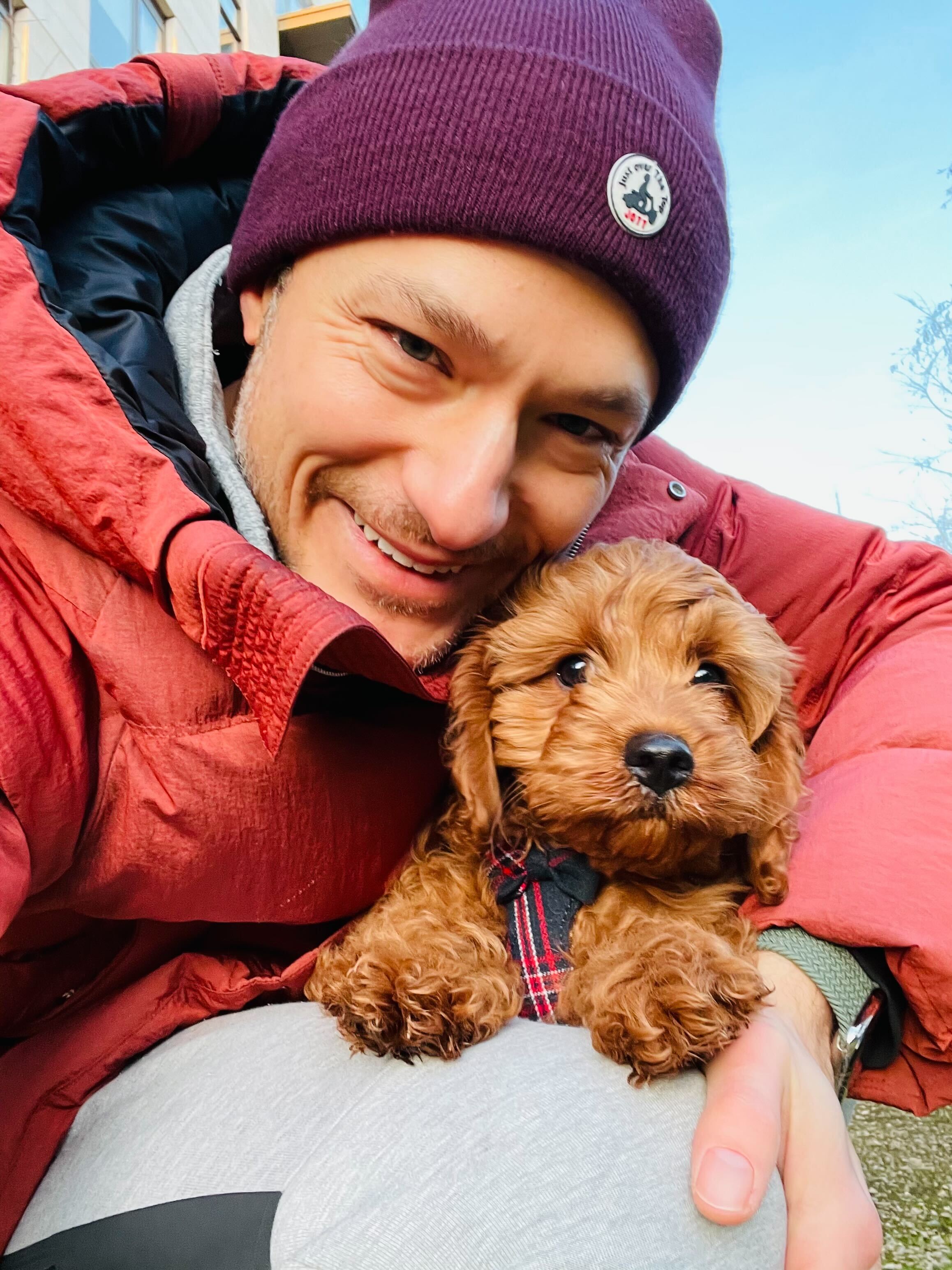 Person in a red jacket holding a small brown dog outdoors.