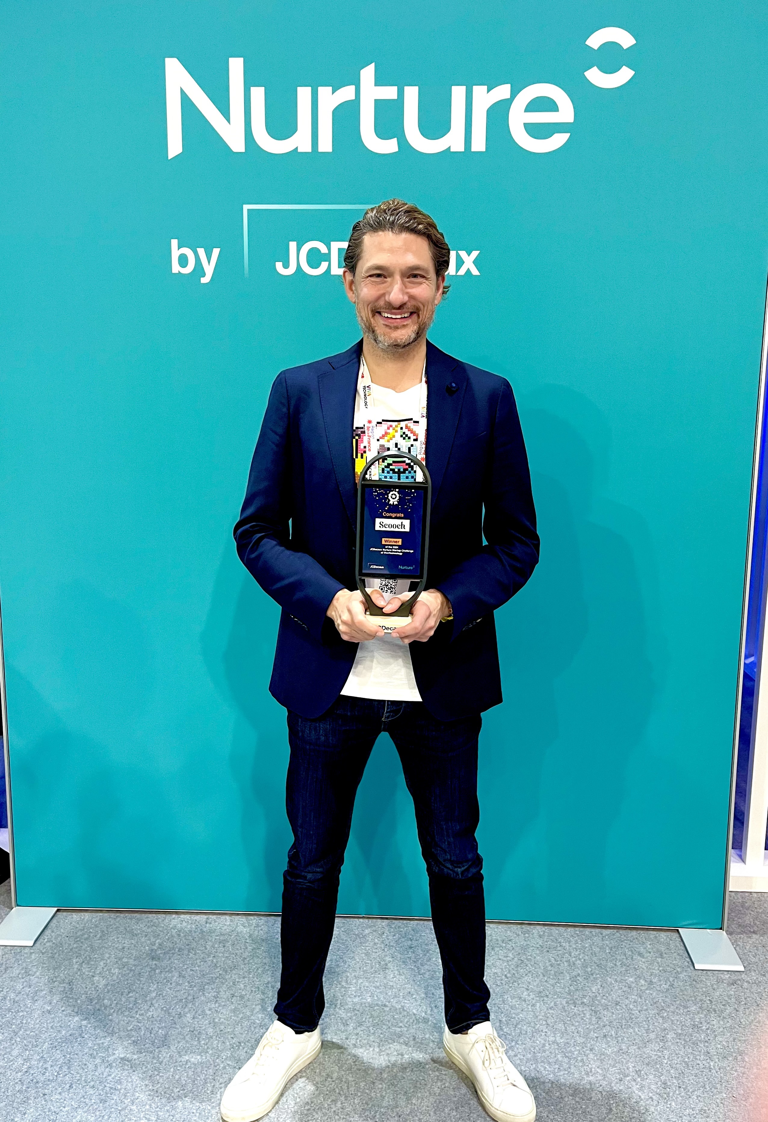 Person holding an award in front of a teal background with 'Nurture' text.