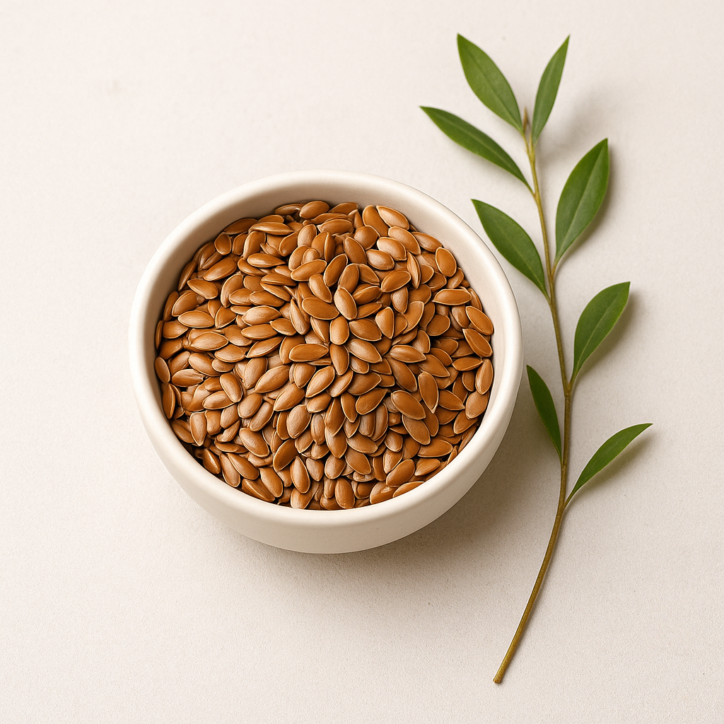 Bowl of brown seeds next to a green leafy branch on a white background.