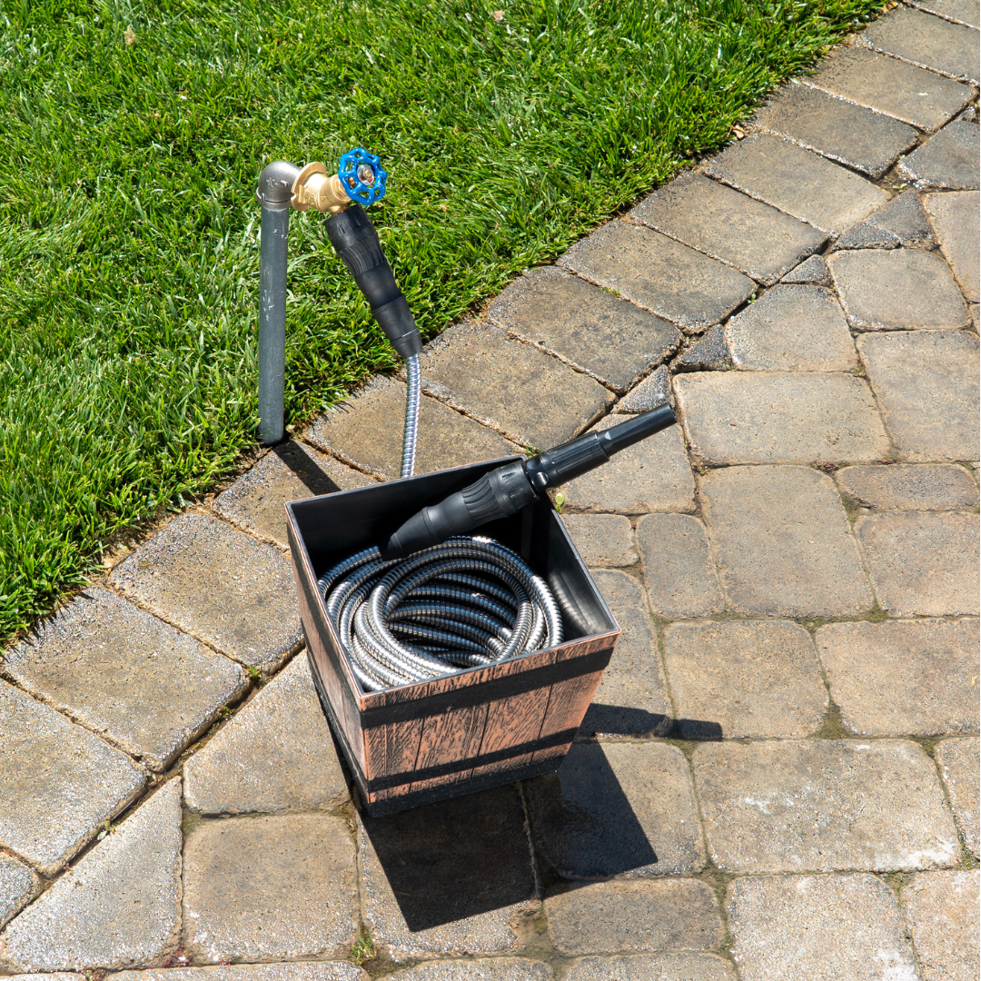 Coiled metal hose in a wooden box on a stone patio near grass.