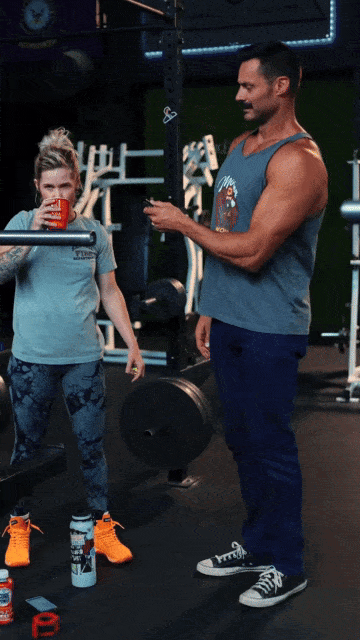 Two people in a gym, one drinking from a red cup, the other holding a phone.