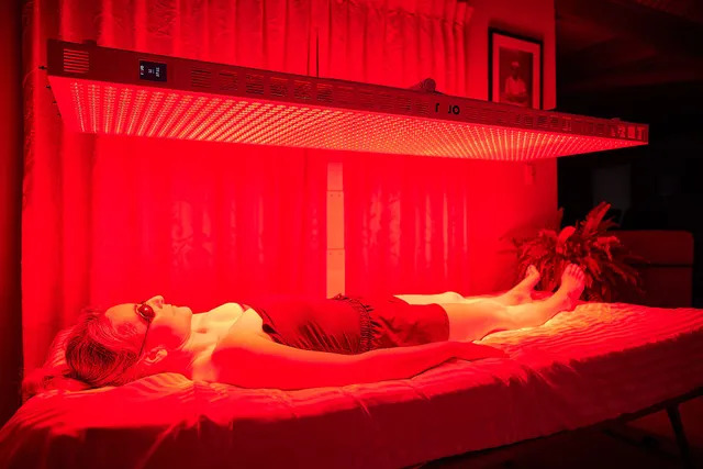 Person lying under a red light therapy device in a dimly lit room.