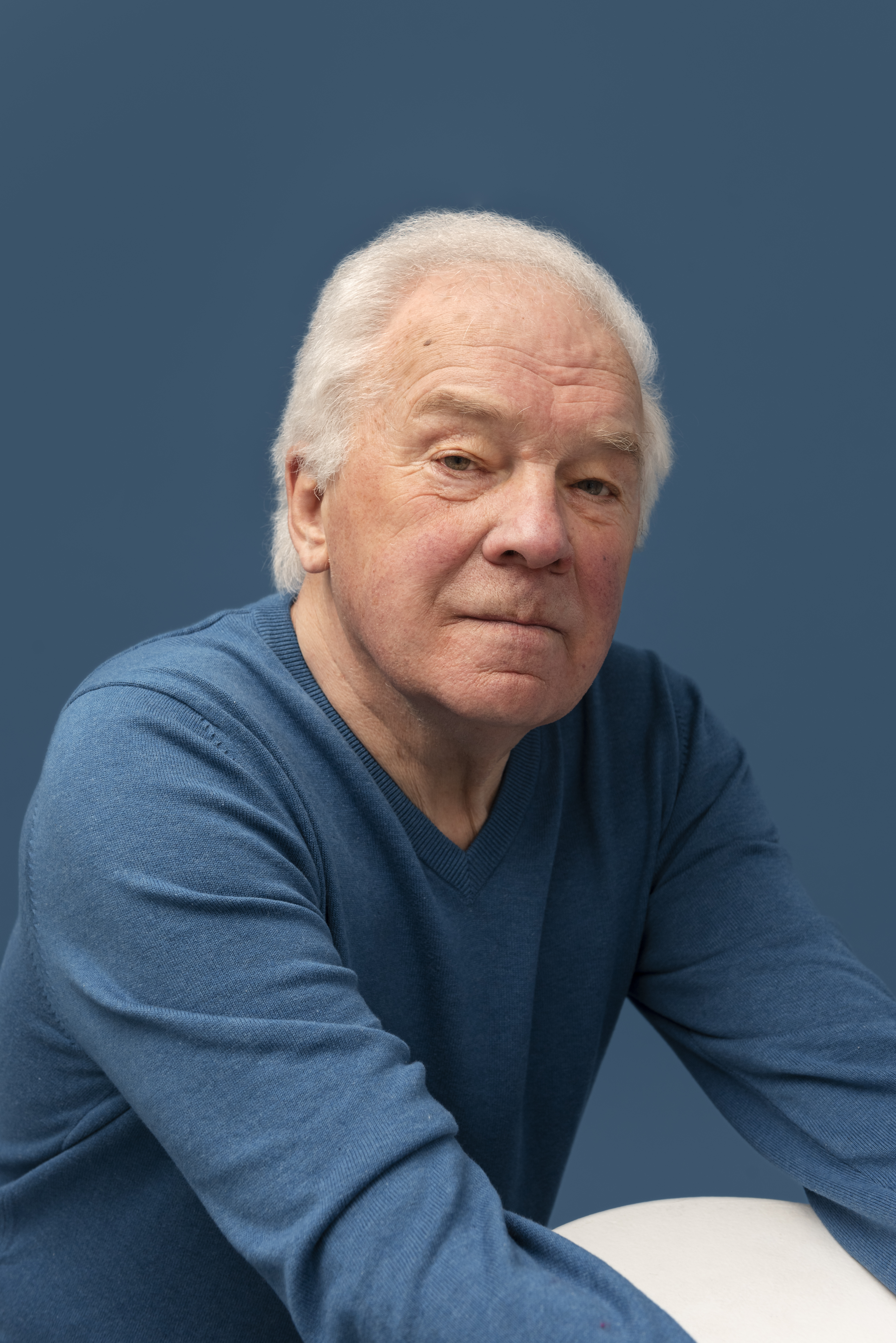 Elderly man in a blue sweater against a blue background.