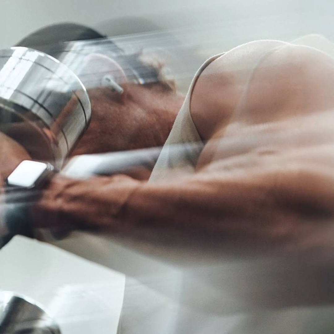 A motion-blurred, close-up photo of a muscular person in a tank top lifting a chrome dumbbell.