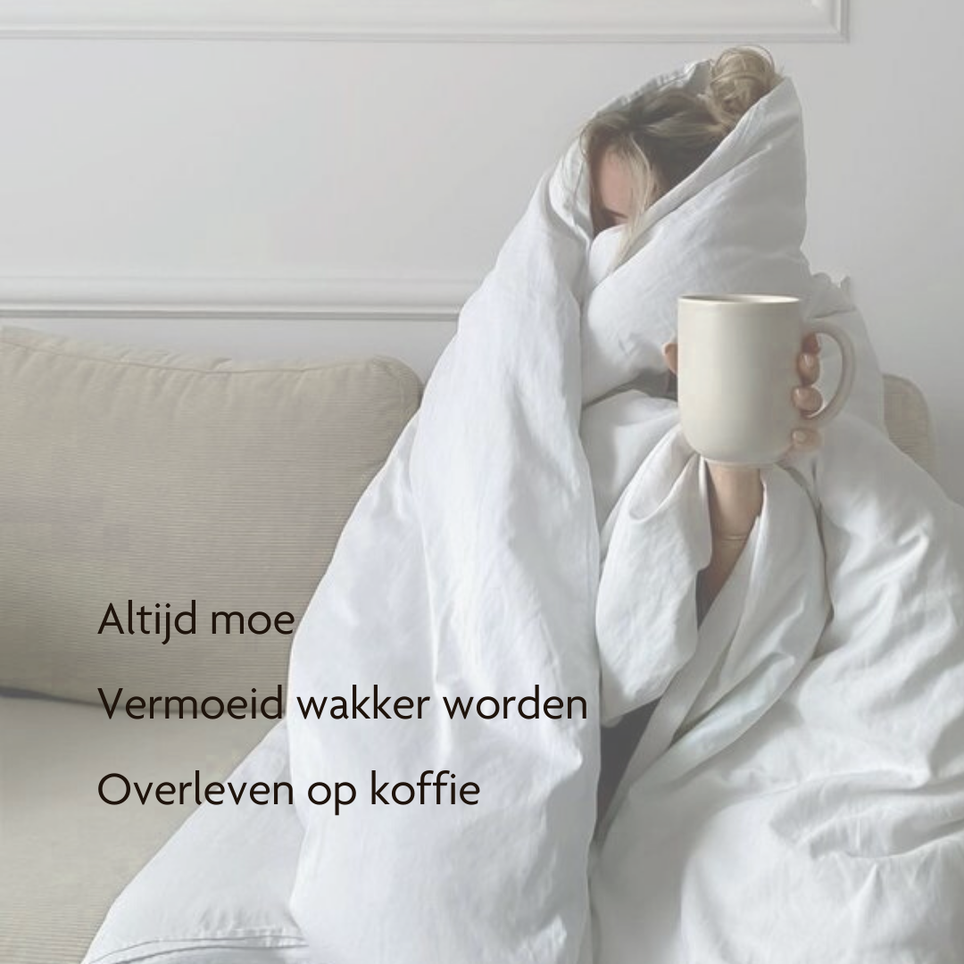 A person completely wrapped in a white duvet sits on a couch holding a beige mug.