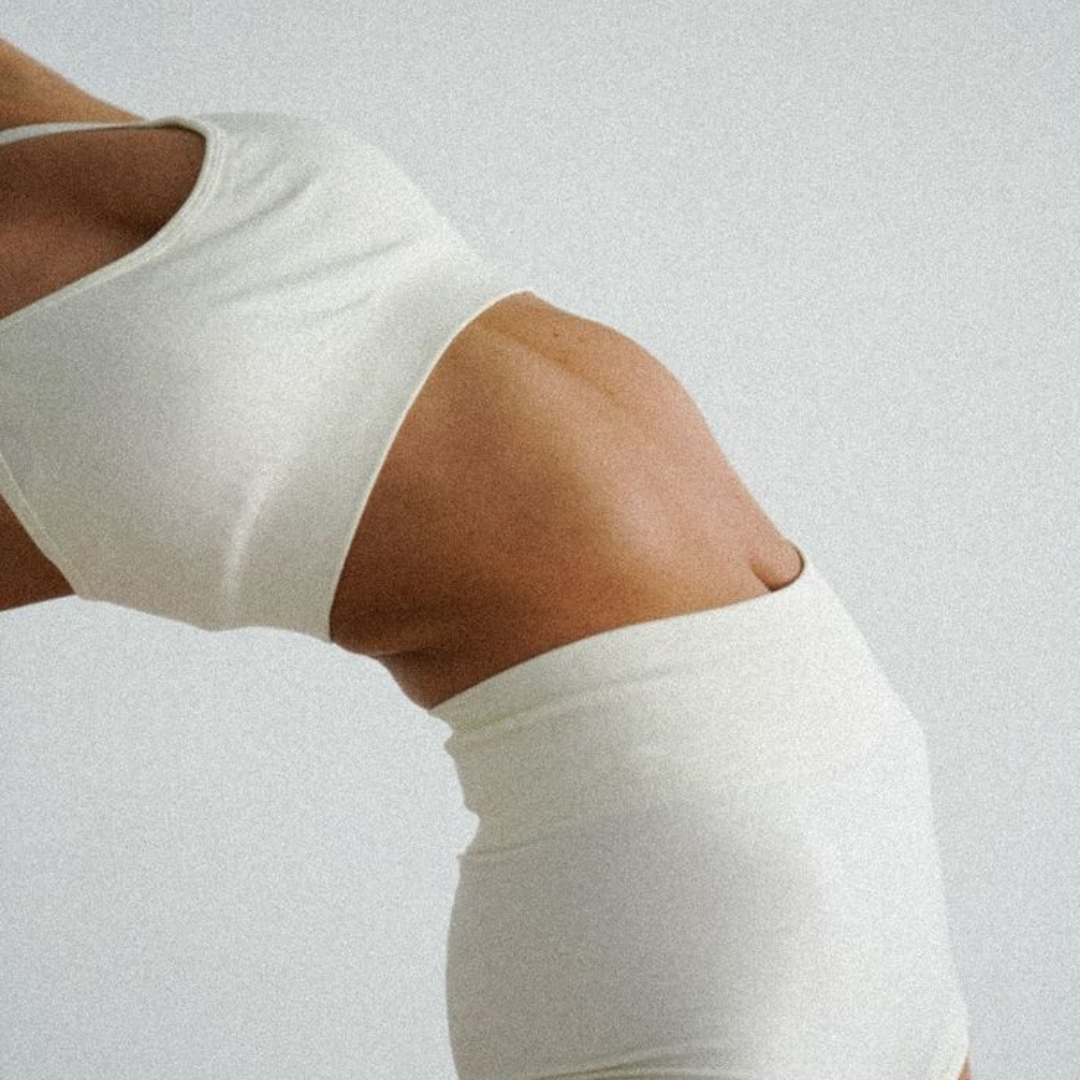 A close-up of a person's toned midsection in a white two-piece outfit, arching their back.