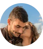 A circular photo of a woman kissing a man on the cheek outdoors.