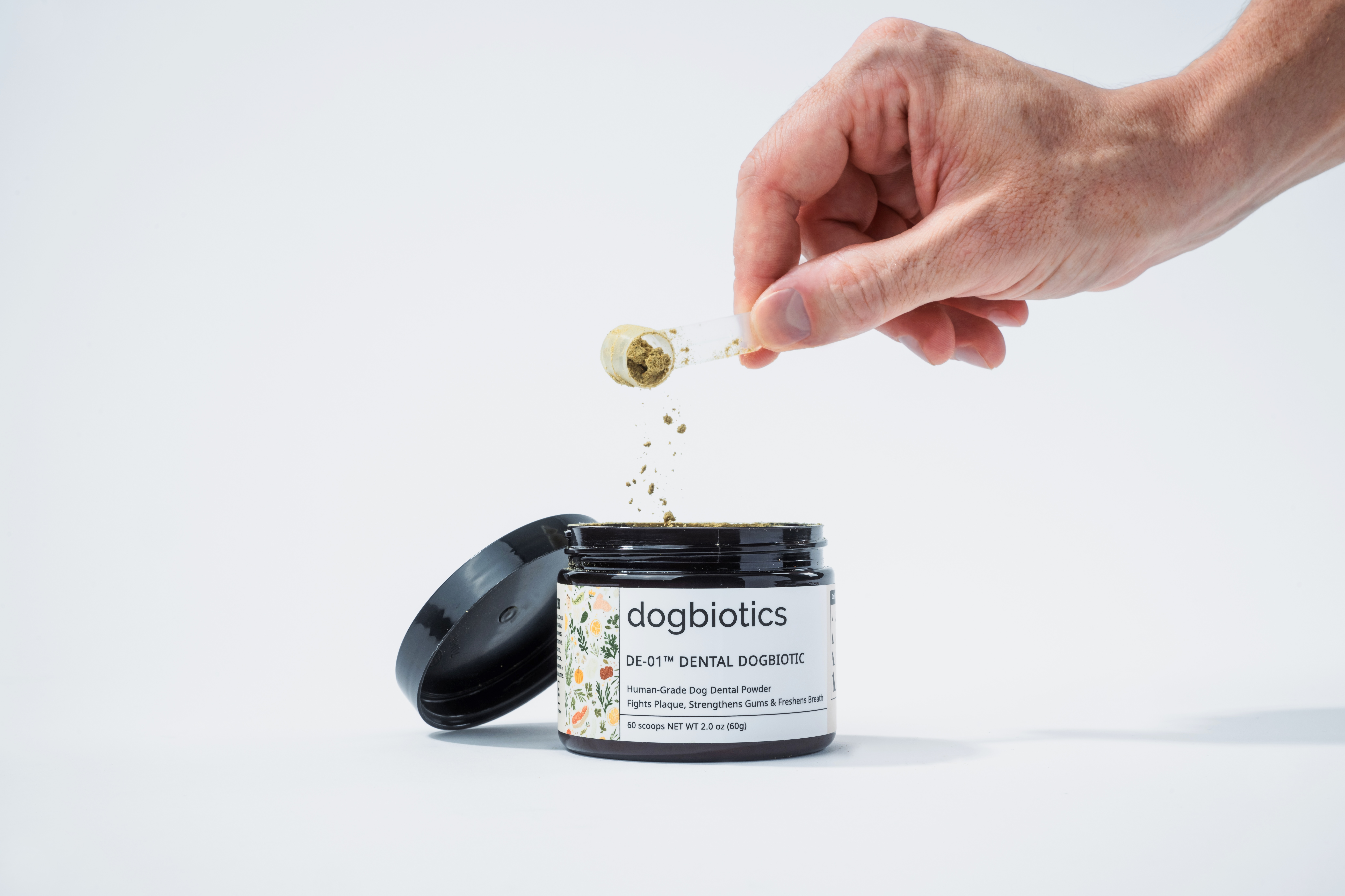 Hand sprinkling powder into an open container labeled 'dogbiotics' on a white background.