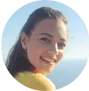 A circular headshot of a smiling woman with dark hair, wearing a yellow shirt outdoors.