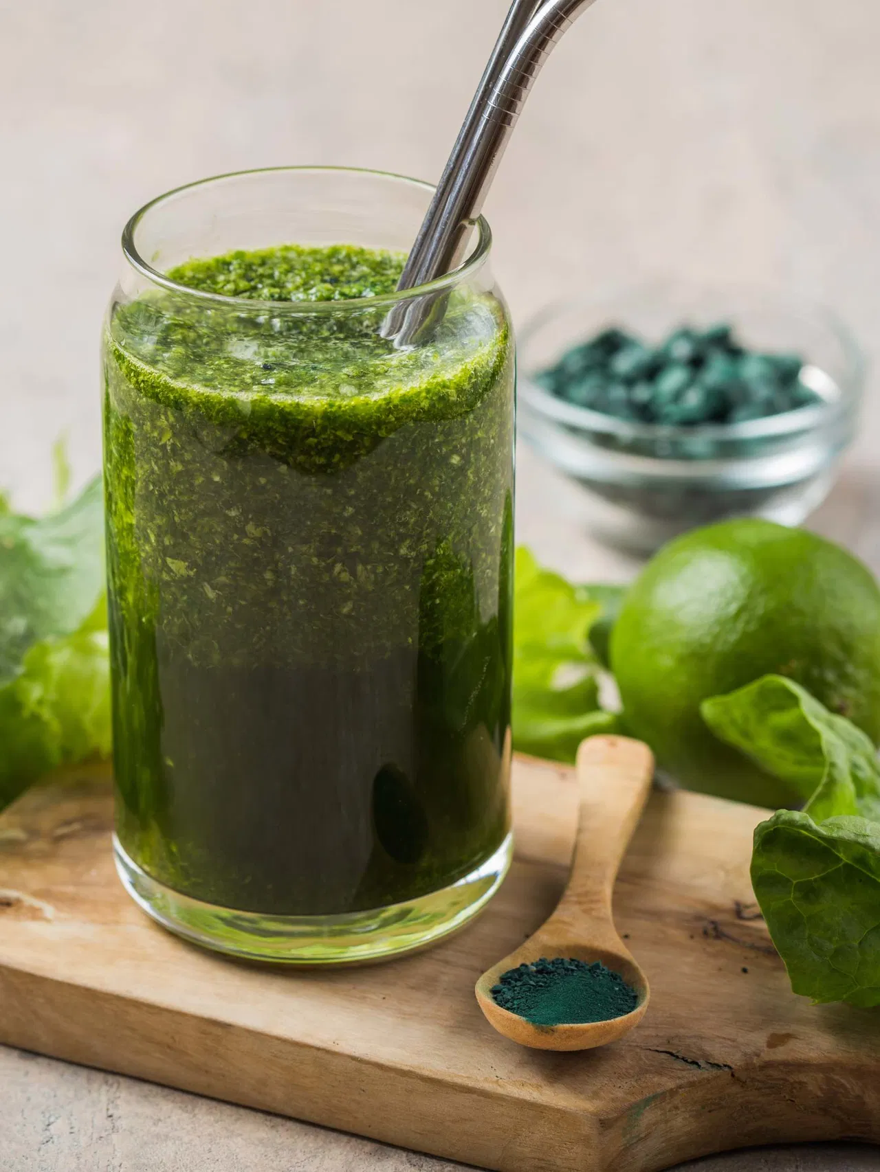 Green juice with metal straw, surrounded by lime and green leaves.