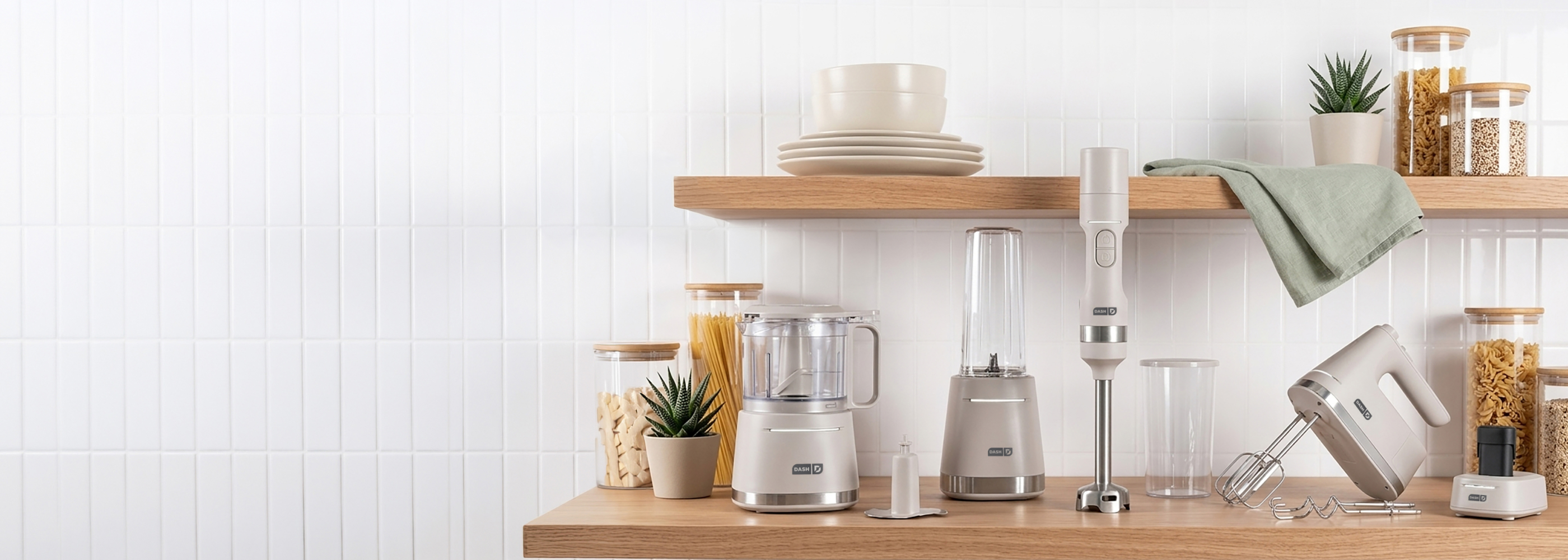 A collection of grey Dash brand kitchen appliances on a white countertop against a white tile wall.