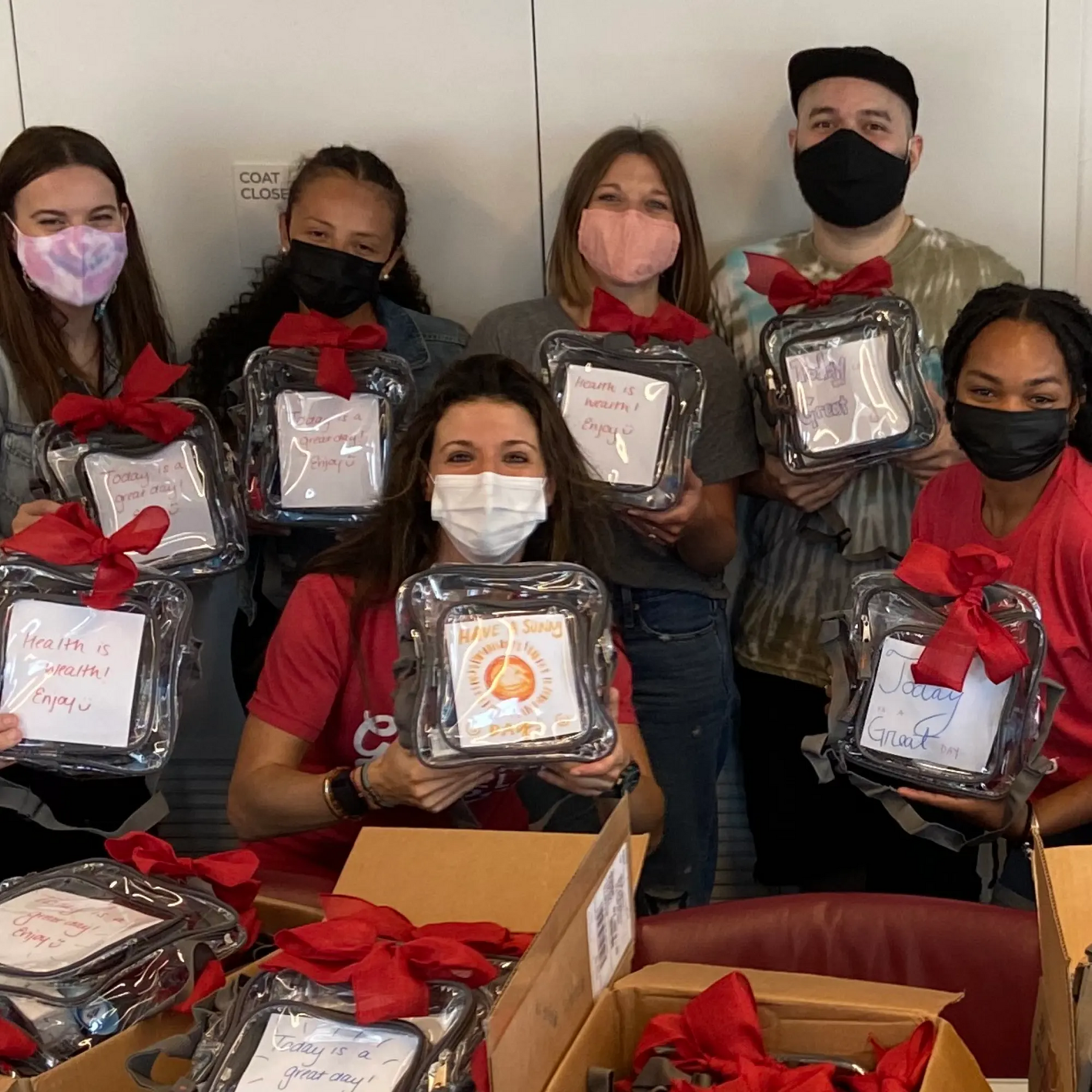 Team members proudly holding care packages with handwritten notes and red bows, supporting the Rise by Dash community initiative.