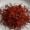 A small pile of red saffron threads sits on a light-colored, textured surface.
