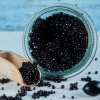 A clear glass jar of black caviar with a small wooden scoop resting beside it.