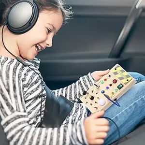 Child wearing headphones, smiling, holding a colorful play board on an airplane seat.