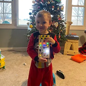 Child in red pajamas holding a toy in front of a decorated Christmas tree.