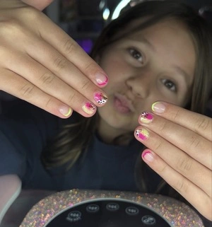 Child displaying colorful nail art with polka dots and floral designs.