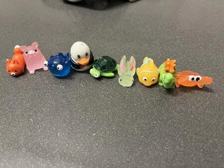 A row of nine small, colorful, translucent animal figurines lined up on a grey surface.