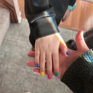 Hands with rainbow light and colorful painted nails.