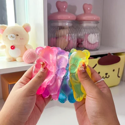 A person's hands holding several colorful, translucent, bear-shaped objects, with cute items in the background.