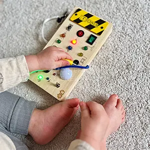 Child playing with a sensory board featuring buttons and lights on a carpeted floor.